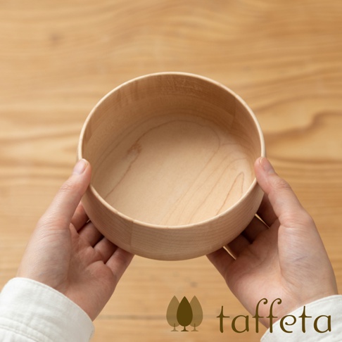 一雙手捧著一個淺色的圓形楓木沙拉碗，碗身光滑，有細緻的木紋，碗內呈現自然的淺木色。