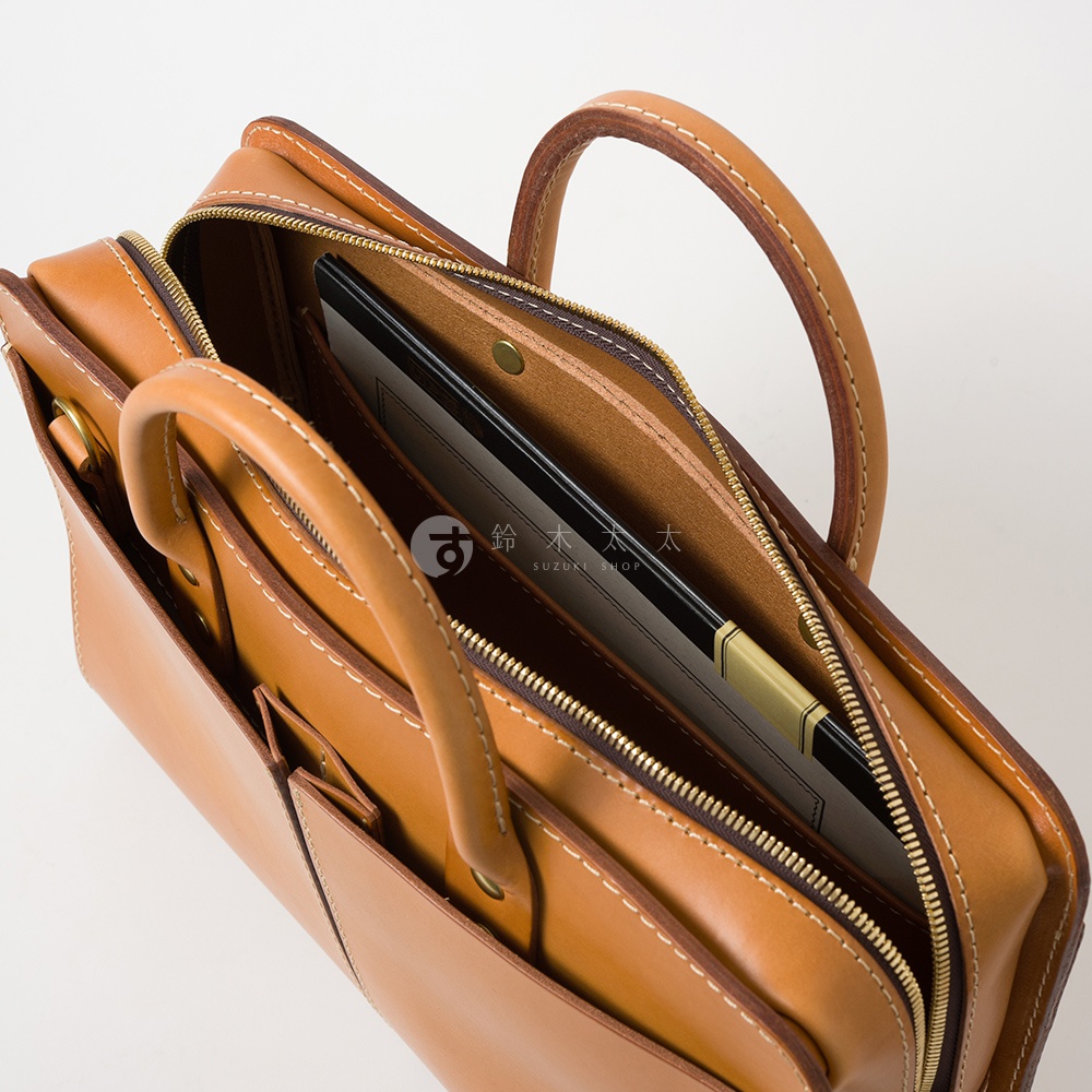 職人手作皮革雙口袋兩用商務公事包，焦糖棕色，以縫線勾勒出包款線條，內部可見文件夾，整體呈現簡約而精緻的質感。