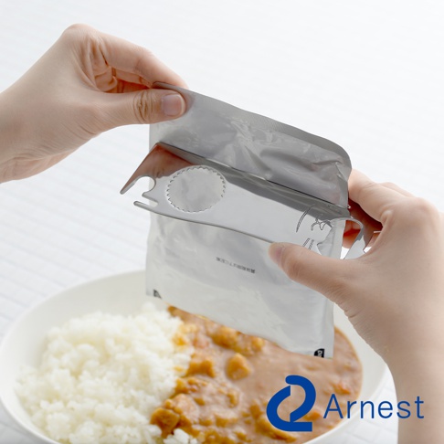 銀色金屬貓咪萬用開罐器，夾住鋁箔食品包，準備倒入白色碗中的米飯和咖哩。