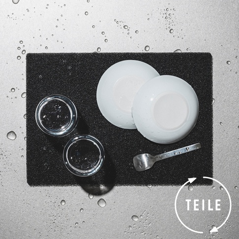 黑色速乾瀝水墊上擺放著兩個白色圓盤、兩個透明玻璃杯及一把金屬湯匙，周圍散落著水珠。