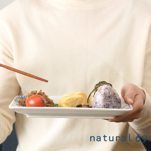 白色長方餐盤盛有日式料理，包含飯糰、玉子燒、番茄和漬物，盤邊印有藍色日式紋飾。