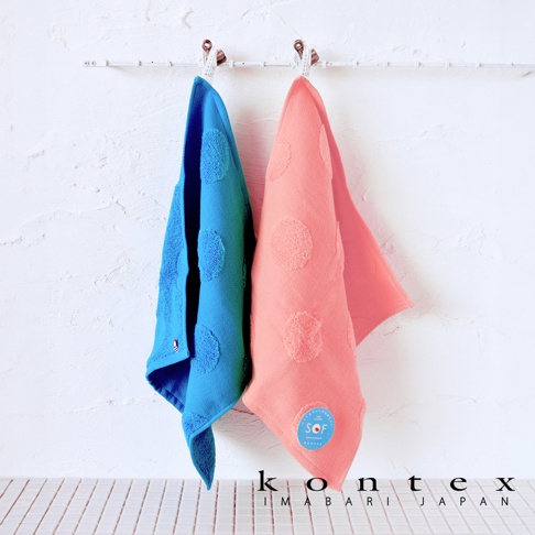 藍色與粉色紗布材質的浴巾，分別以圓點緹花裝飾，並用掛勾懸掛於白色牆面上。