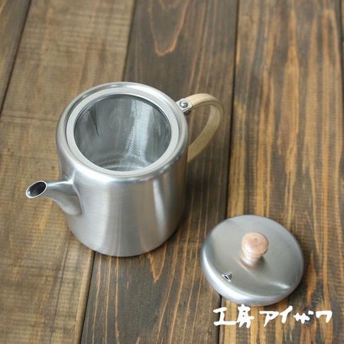 霧面不鏽鋼直筒茶壺，帶有側邊木質手柄，壺嘴細長，內部有濾網。一旁擺放著同樣材質的圓形壺蓋，頂部有木質提鈕。