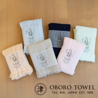 六條三層紗純棉輕柔戶外掛脖毛巾，顏色包含淺藍、深藍、米白、米黃、淺粉紅，材質輕薄，帶有流蘇邊緣，每條毛巾皆附有產品標籤。