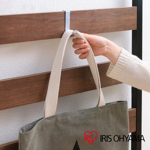 一隻手正將一個米色帆布提袋掛在一個銀色金屬掛鉤上，該掛鉤固定在木紋層架上。