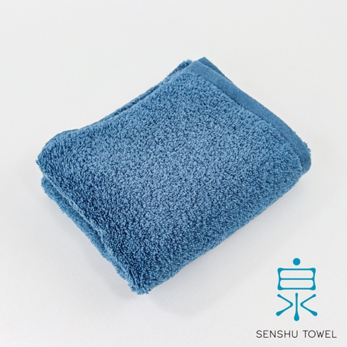 藍色長纖毛巾，質地柔軟，毛圈豐盈，呈現高吸水特性。毛巾對折，一角露出品牌標誌「泉」及「SENSHU TOWEL」。