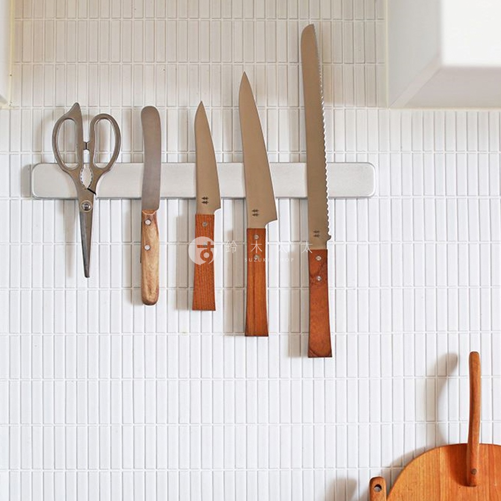 morinoki / Ban nou knife 萬用刀，一套包含銀色金屬刀刃與木質手柄的廚房刀具，包括一把剪刀、兩把直刀刃的刀，以及兩把鋸齒刀刃的刀，整齊陳列於廚房磁性刀架上，背景為白色縱向磁磚牆面。