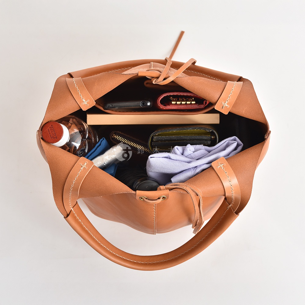 職人手作皮革球形肩掛托特包，以咖啡色皮革製成，包內裝有手機、錢包、鑰匙包、瓶裝水、摺疊傘和衣物。