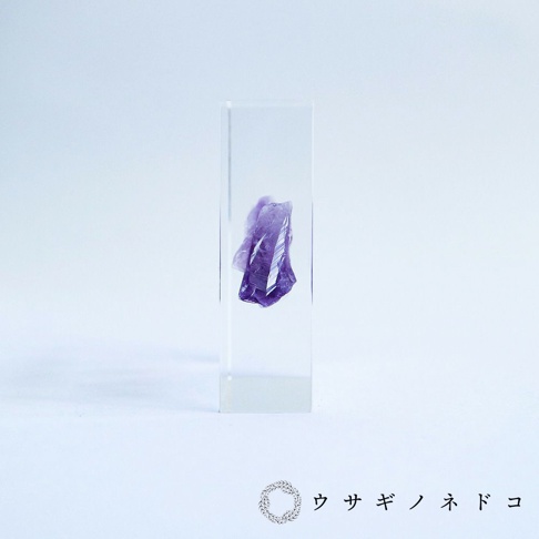 透明壓克力方塊中封存著一塊紫色紫水晶晶體，晶體呈現不規則的切面，部分區域透光。