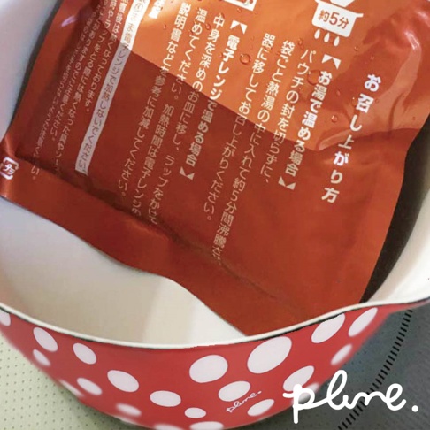 紅色琺瑯單柄牛奶鍋，鍋身外側印有白色圓點圖案，鍋內有一個橘紅色包裝的食品。