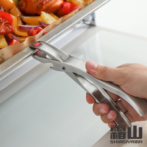 一只手正握著一個銀色304不鏽鋼製的防燙取碗夾，夾著一個裝有烤雞和蔬菜的烤盤邊緣。取碗夾有紅色的防滑點，整體呈現金屬光澤。