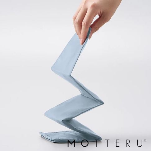 淺藍色輕時尚束口摺疊隨行袋，由布料製成，呈現Z字形摺疊狀態，一隻手正在提起袋子的頂部。