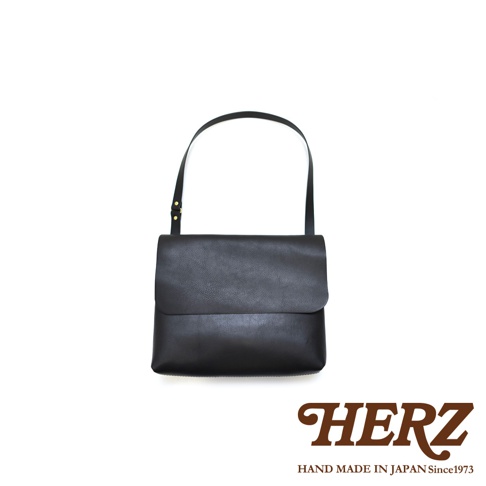 黑色皮革經典郵差包，帶有可調節的細肩帶，包身為簡潔的方形設計，翻蓋式封口。