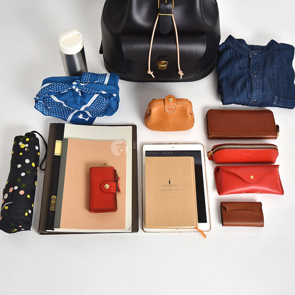 黑色皮革後背包，搭配多種配件：藍色印花布包、咖啡色與紅色皮革長夾、筆記本、紅色皮革零錢包、白色保溫瓶、牛仔襯衫，以及黑色圓點摺疊傘。