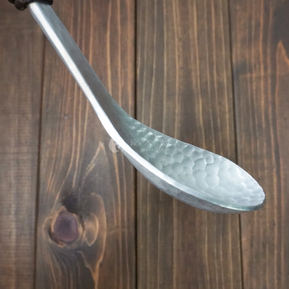 鋁製湯勺，勺面帶有錘目紋，勺柄為木質，置於木紋背景上。