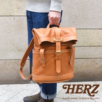 棕色皮革製雙口袋折蓋後背包，配有金屬扣環和車縫線細節，由人攜帶。