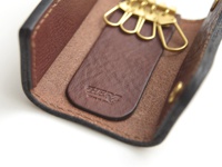 職人手作皮革鑰匙包，外層黑色皮革，內層咖啡色皮革，內有四個金色鑰匙扣和一個品牌壓印的皮革條。