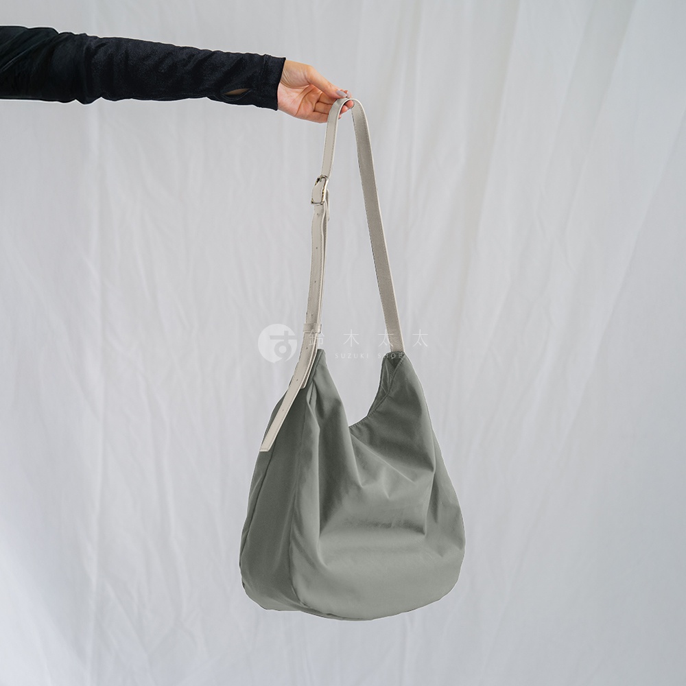 Atelier nuu 品牌灰色尼龍斜肩包，以白色斜肩帶搭配，包身呈現柔軟垂墜感，適合搭配各種風格服飾。