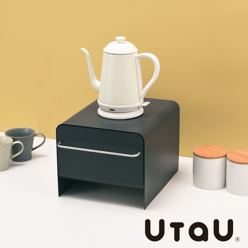 深灰色抽屜式萬用收納整理櫃，帶有銀色金屬把手，櫃頂放置著一個米白色電熱水壺。畫面右側有兩個白色圓形收納罐，罐蓋為木質。