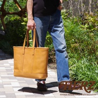 淺棕色皮革經典托特包，方形包身，雙提把，包包正面有兩條垂直縫線裝飾，底部加寬，材質為皮革。