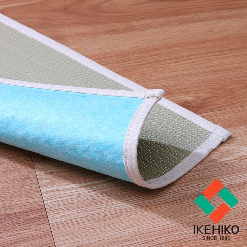 藺草抗菌除臭枕墊，一側為淺綠色藺草編織材質，另一側為淺藍色無紡布材質，邊緣有白色布條包邊，平鋪於木質地板上。