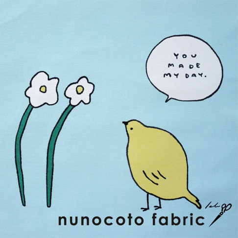 淺藍色帆布材質，左側有兩朵白色小花，花莖為綠色。右側有一隻黃色小鳥，頭頂上方有一個對話氣泡，氣泡內寫著「YOU MADE MY DAY.」，下方有「nunocoto fabric」字樣。