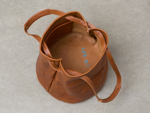 棕色皮革抽繩肩背包，具有皮革提把和抽繩開口，內部印有藍色數字標記。