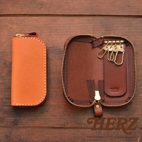 兩個棕色皮革鑰匙包，一個閉合，另一個打開展示四個金屬鑰匙鉤，背景為木紋桌面。