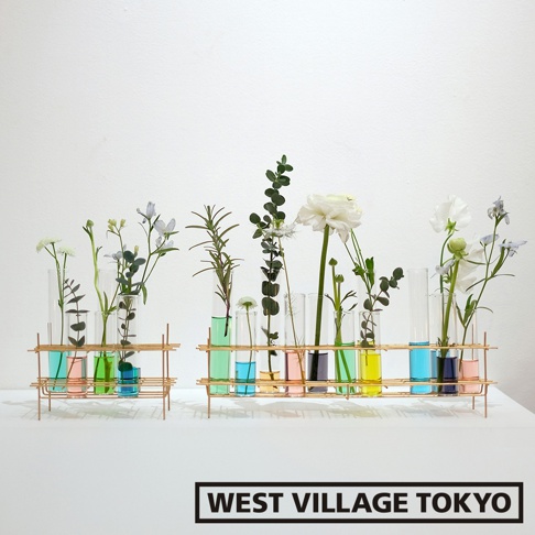 展示兩個金色金屬支架，各承載一排玻璃試管花器，試管內裝有不同顏色的液體及各式綠葉與花朵，整體呈現簡約現代的風格。