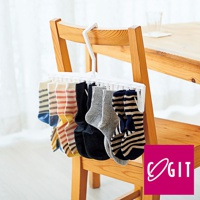 白色塑膠晾衣夾，掛有十雙不同花色、材質的襪子，包括條紋、純色等，夾子上方有掛鉤，懸掛於木椅上。