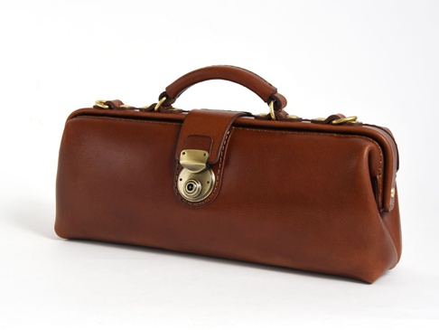 職人手作皮革橫長形杜勒斯單肩包，以咖啡棕色皮革製成，設有金色金屬旋鎖扣和手提把，整體風格經典復古。