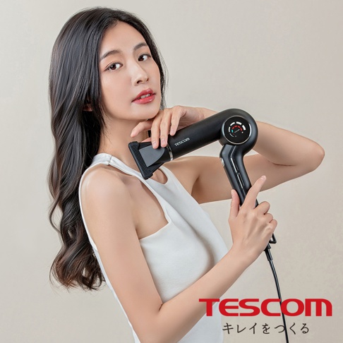 一位年輕女子手持黑色TESCOM吹風機，吹風機上印有品牌名稱，並有一個圓形指示儀。