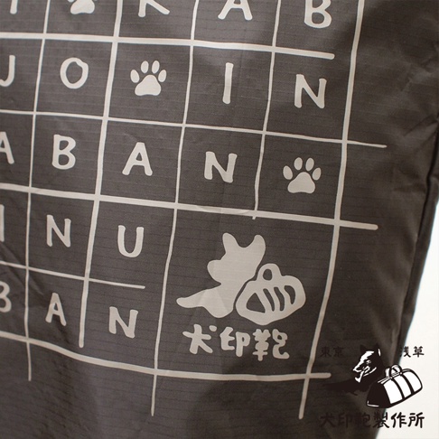 深灰色環保折疊收納購物袋，表面印有白色網格、字母、狗爪圖案及「犬印鞄」品牌標誌，材質為尼龍。