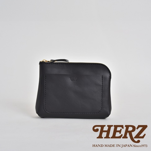 黑色皮革小物收納包，附有拉鍊開合和前方貼袋，皮革材質，有職人品牌標誌。