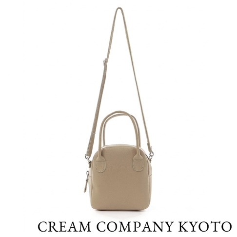 這是一款 CREAM COMPANY KYOTO 的駝色皮革兩用貝殼包，具備手提把與可拆卸式肩背帶，外型簡約輕巧，呈現出質感細膩的荔枝紋皮革紋理，適合日常穿搭使用。