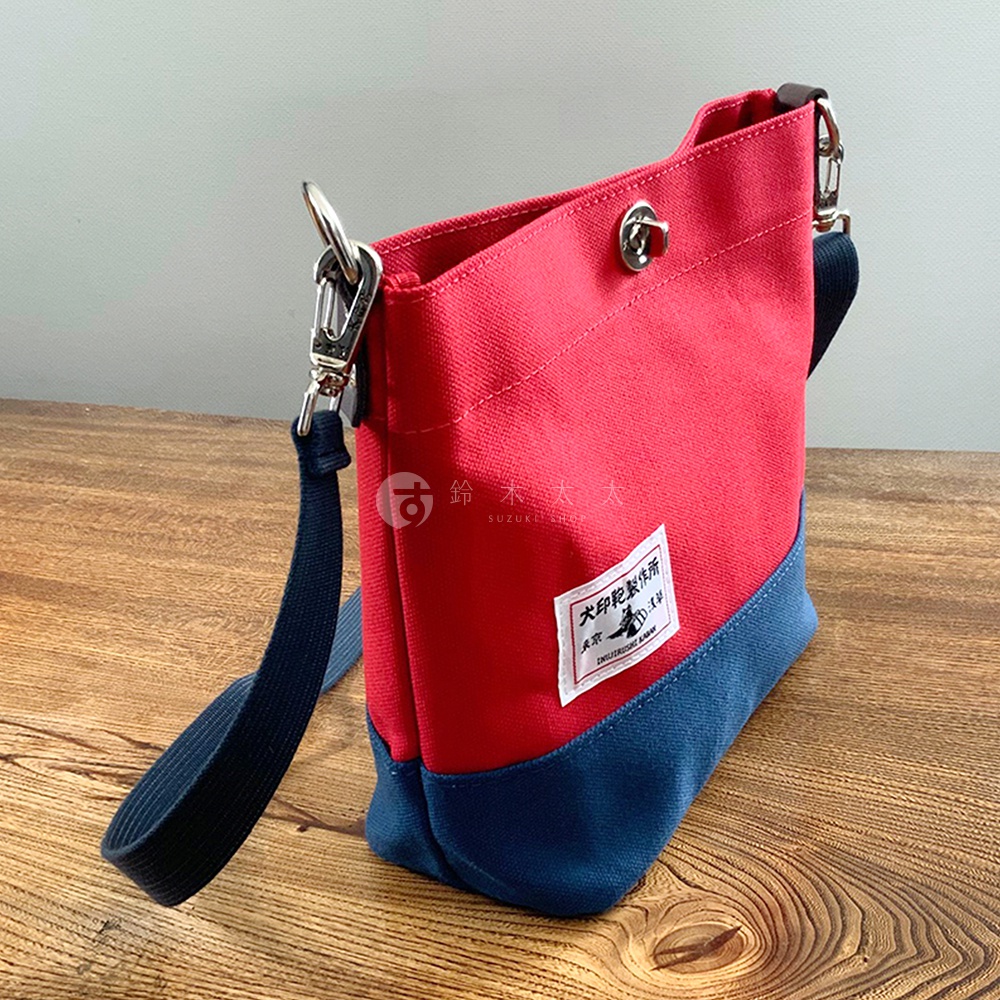 犬印純綿帆布雙色迷你側背包，主體為紅色，底部為深藍色，配有深藍色織帶和銀色金屬扣環。