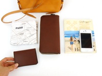 職人手作皮革散步直式單肩包 (CP-3) 展現其全貌，包含一個焦糖色皮革單肩包、一個咖啡色皮革長夾、一個咖啡色皮革名片夾，以及一張印有巴黎地圖的白色布巾和一本旅遊雜誌，旁置著一支白色手機。