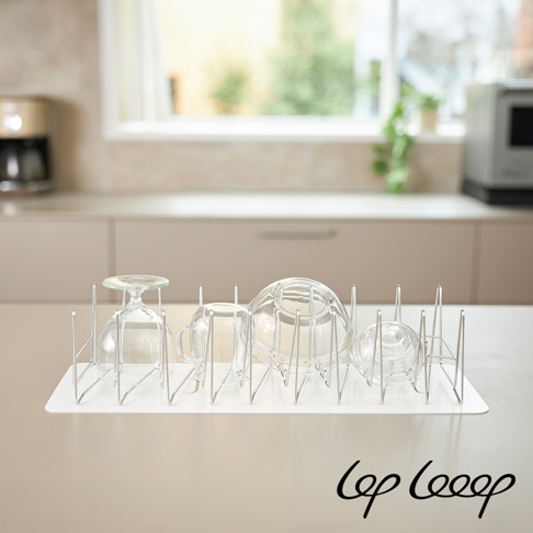 伸縮式不鏽鋼瀝水架，架身為銀色金屬材質，搭配白色防水墊，架上放置數個玻璃杯和碗。