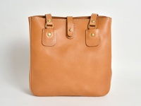 淺棕色皮革製的職人手作托特包，配有兩條短提把、一個中央磁扣封口，以及兩側的裝飾性壓扣設計。