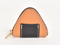 職人手作皮革零錢包，呈三角飯糰造型，主體為淺棕色皮革，中央區域為黑色皮革拼接，邊緣以白色縫線裝飾，並配有金色拉鍊。