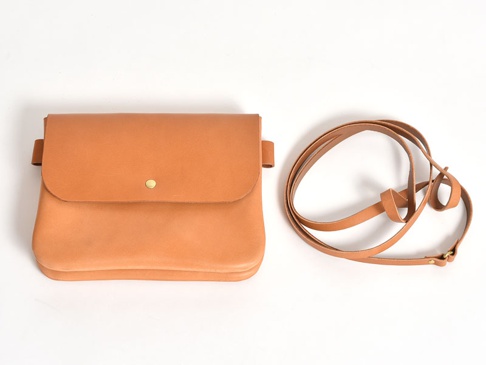 職人手作皮革直式隨行袋 (CP-9)，呈現自然棕色調，以柔軟皮革製成，帶有金屬鈕扣開合，並配有一條可調整長度的皮革長背帶。