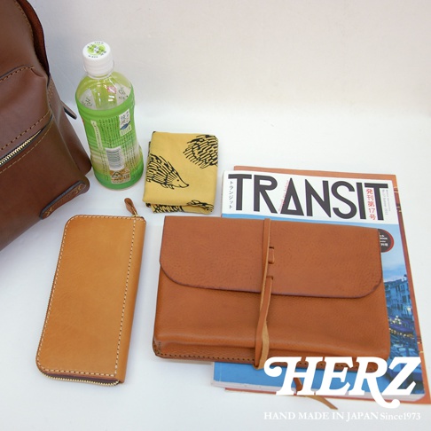 棕色皮革長夾、黃色刺蝟圖案手帕、一本雜誌（「TRANSIT」字樣）、一瓶綠色飲料，以及部分褐色皮革後背包。