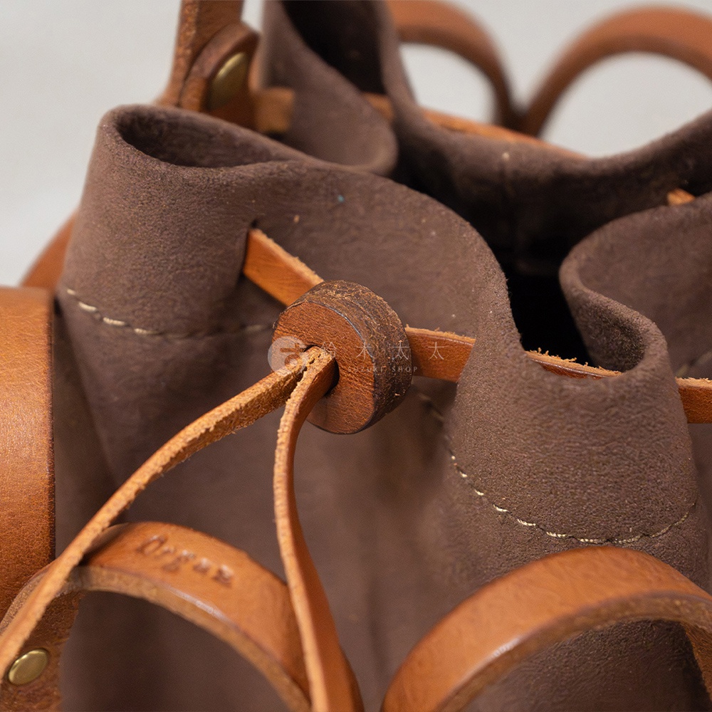 日本HERZ職人手作皮革Organ編織水桶包，特寫近觀，展示棕色麂皮與皮革材質的編織細節、抽繩與圓形皮革拉環，以及皮革上壓印的Organ品牌字樣。