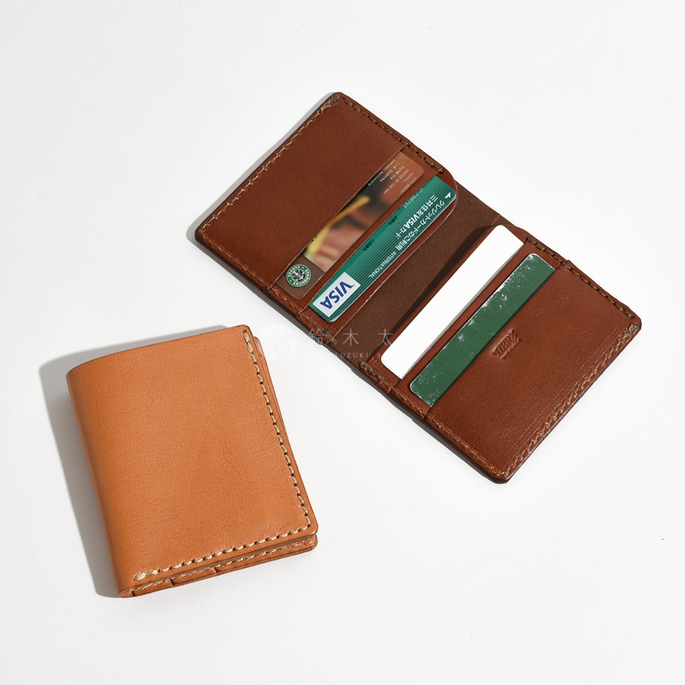 一棕褐色皮革對折式卡片夾，內有兩張卡片，一張為VISA卡，一張為綠色卡片，旁邊另有一個小巧的淺棕色皮革皮夾。