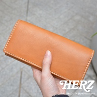 一只手拿著駝色軟皮長夾，夾子邊緣有白色縫線。