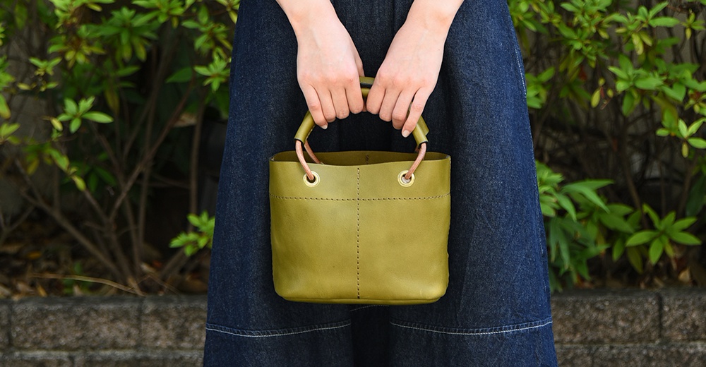 橄欖綠色皮革手提午餐袋，配有圓形加厚提把，設計簡約，適合日常攜帶。