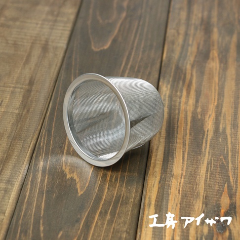 不鏽鋼濾網茶葉過濾器，為圓柱形，細網孔，銀色，置於木紋背景上。
