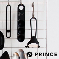 黑色削皮器，設有彎曲的黑色手柄和銀色刀片，掛在金屬網架上。