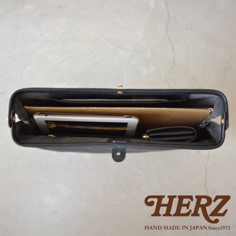 黑色皮革手拿包，內部裝有平板電腦、筆記本和零錢包，包包有金屬扣環和磁扣。