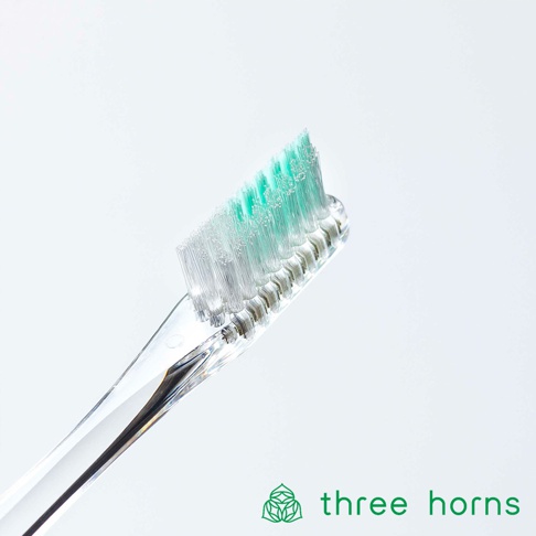 透明塑膠柄的牙刷，刷頭有綠色與白色柔毛，呈傾斜角度，背景為純白色。